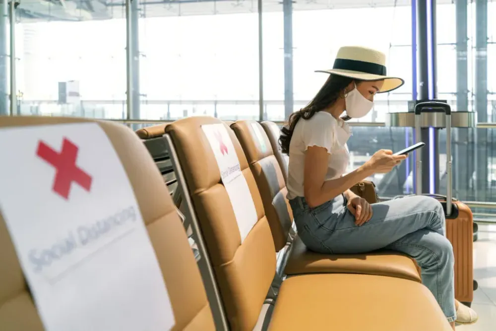 Woman wearing a mask, waiting in social distanced airport terminal